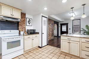 Kitchen with cream cabinetry, white electric range, under cabinet range hood, arched walkways, and black microwave