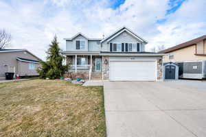 Traditional home featuring a porch, concrete driveway, stone siding, and a front yard