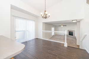 Interior space featuring ceiling fan with notable chandelier, wood finished floors, a fireplace, baseboards, and vaulted ceiling