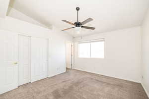Unfurnished bedroom with baseboards, vaulted ceiling, carpet flooring, a closet, and a ceiling fan