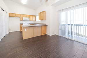 Kitchen featuring white appliances, lofted ceiling, a peninsula, and dark wood finished floors