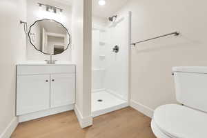 Bathroom with toilet, wood finished floors, baseboards, walk in shower, and vanity