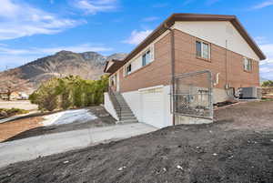 View of property exterior featuring central air condition unit, a mountain view, stairway, an attached garage, and brick siding