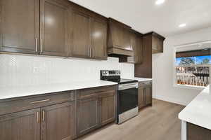 Kitchen featuring tasteful backsplash, premium range hood, light countertops, stainless steel range with electric cooktop, and light wood-style floors