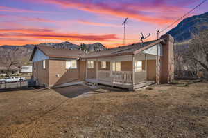 Back of house at dusk with brick siding, a porch, central AC, a chimney, and a mountain view