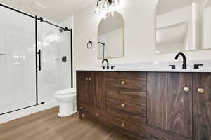 Full bath featuring a shower stall, toilet, double vanity, wood finished floors, and a sink