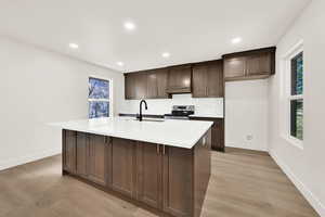 Kitchen featuring a sink, stainless steel electric range, a kitchen island with sink, and light wood finished floors