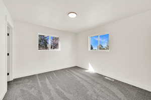 Unfurnished room with visible vents, baseboards, and dark carpet