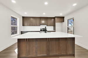 Kitchen featuring tasteful backsplash, a sink, light countertops, a large island, and dark wood-style flooring