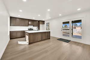 Kitchen with light wood-type flooring, stainless steel range with electric stovetop, a kitchen island with sink, a sink, and light countertops