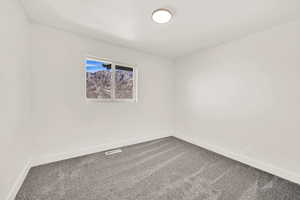 Unfurnished room with visible vents, baseboards, and dark carpet