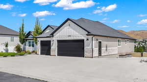 Modern inspired farmhouse featuring stone siding, board and batten siding, an attached garage, and driveway