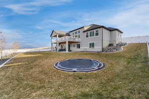 Back of house with a trampoline, a fenced backyard, a yard, and stucco siding
