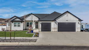 Modern farmhouse with driveway, roof with shingles, a front lawn, a garage, and board and batten siding. Grass has been edited because of the season.