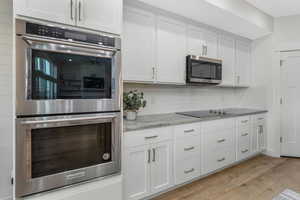 Kitchen with decorative backsplash, white cabinets, stainless steel appliances, and light wood-type flooring