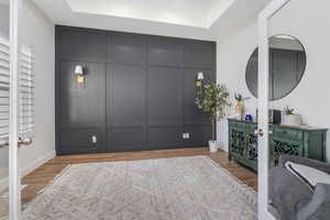Interior space with a tray ceiling, a decorative wall, french doors, and light wood-type flooring