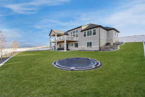 Rear view of house with a yard, a fenced backyard, stucco siding, and a trampoline. Grass is edited for the season