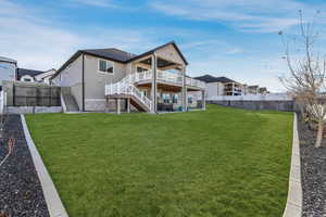 Back of house featuring stairs, a lawn, a deck, a fenced backyard, and a patio area, fruit trees. Grass is edited for the season
