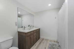 ADU Full bathroom featuring baseboards, toilet, double vanity, wood finished floors, and a sink