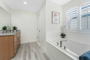 Bathroom with vanity, wood finished floors, baseboards, recessed lighting, and a bath