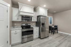 ADU Kitchen with stainless steel appliances, baseboards, light wood-style floors, and white cabinetry