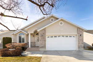 View of front of home with a garage, brick siding, driveway, and stucco siding