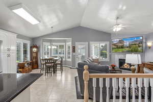 Living area with vaulted ceiling, a tiled fireplace, ceiling fan, light tile patterned floors, and carpeted area