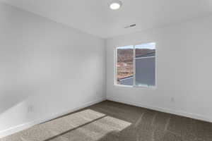 Empty room featuring visible vents, baseboards, and dark colored carpet