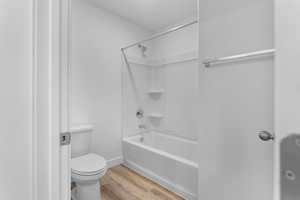 Full bathroom featuring baseboards, toilet, wood finished floors, and  shower combination