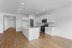 Kitchen featuring light wood-style flooring, a sink, white cabinetry, stainless steel appliances, and light countertops