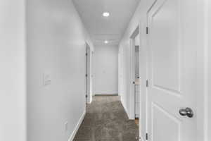 Hall with attic access, baseboards, and dark colored carpet