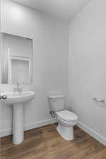 Bathroom with toilet, wood finished floors, baseboards, and a sink