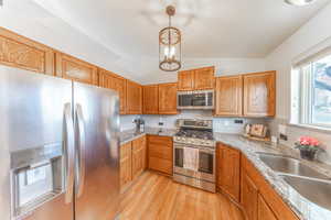 Kitchen with backsplash, light wood-type flooring, vaulted ceiling, appliances with stainless steel finishes, and a sink