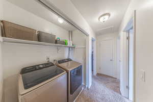 Clothes washing area with a textured ceiling, washing machine and dryer, carpet floors, baseboards, and laundry area