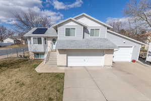 Tri-level home featuring brick siding, fence, concrete driveway, a front yard, and roof mounted solar panels. Solar panels will be paid off by seller at closing.