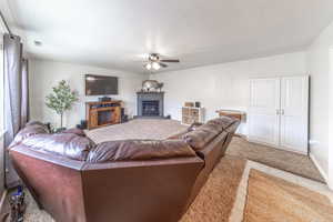 Living area with visible vents, a textured ceiling, ceiling fan, and a glass covered fireplace