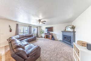 Carpeted living room featuring baseboards, visible vents, ceiling fan, a textured ceiling, and a glass covered fireplace