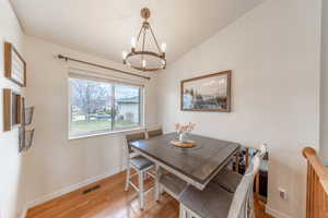 Dining space with visible vents, baseboards, light wood-type flooring, vaulted ceiling, and a notable chandelier