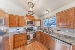 Kitchen with lofted ceiling, appliances with stainless steel finishes, light wood-style floors, brown cabinetry, and a sink