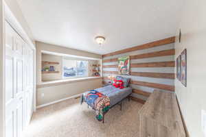 Carpeted bedroom with baseboards, a closet, wood walls, and a textured ceiling