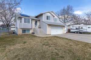 Tri-level home with fence, cooling unit, concrete driveway, a front yard, and solar panels