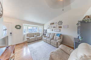 Living area with visible vents, baseboards, lofted ceiling, and light wood-style floors