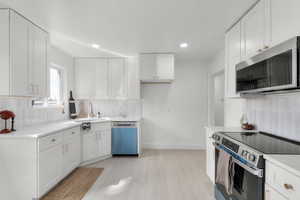 Kitchen featuring a sink, tasteful backsplash, white cabinetry, stainless steel appliances, and light countertops