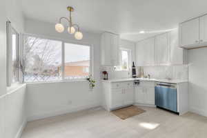 Kitchen with decorative backsplash, white cabinetry, stainless steel dishwasher, and light countertops