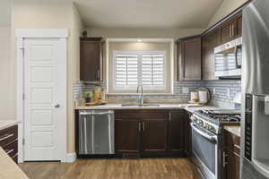 Kitchen with wood finished floors, a sink, light countertops, dark brown cabinets, and appliances with stainless steel finishes