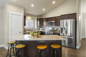 Kitchen featuring a sink, dark brown cabinetry, appliances with stainless steel finishes, light stone countertops, and vaulted ceiling