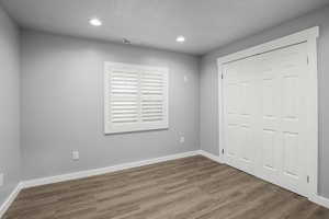 Unfurnished bedroom with a textured ceiling, wood finished floors, visible vents, and baseboards
