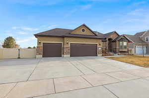 View of front of home featuring concrete driveway, stucco siding, stone siding, an attached garage, and a gate