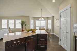 Kitchen featuring light stone counters, baseboards, dark wood finished floors, dark brown cabinets, and a chandelier