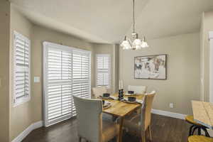 Dining space featuring a notable chandelier, lofted ceiling, a textured ceiling, baseboards, and dark wood-style flooring